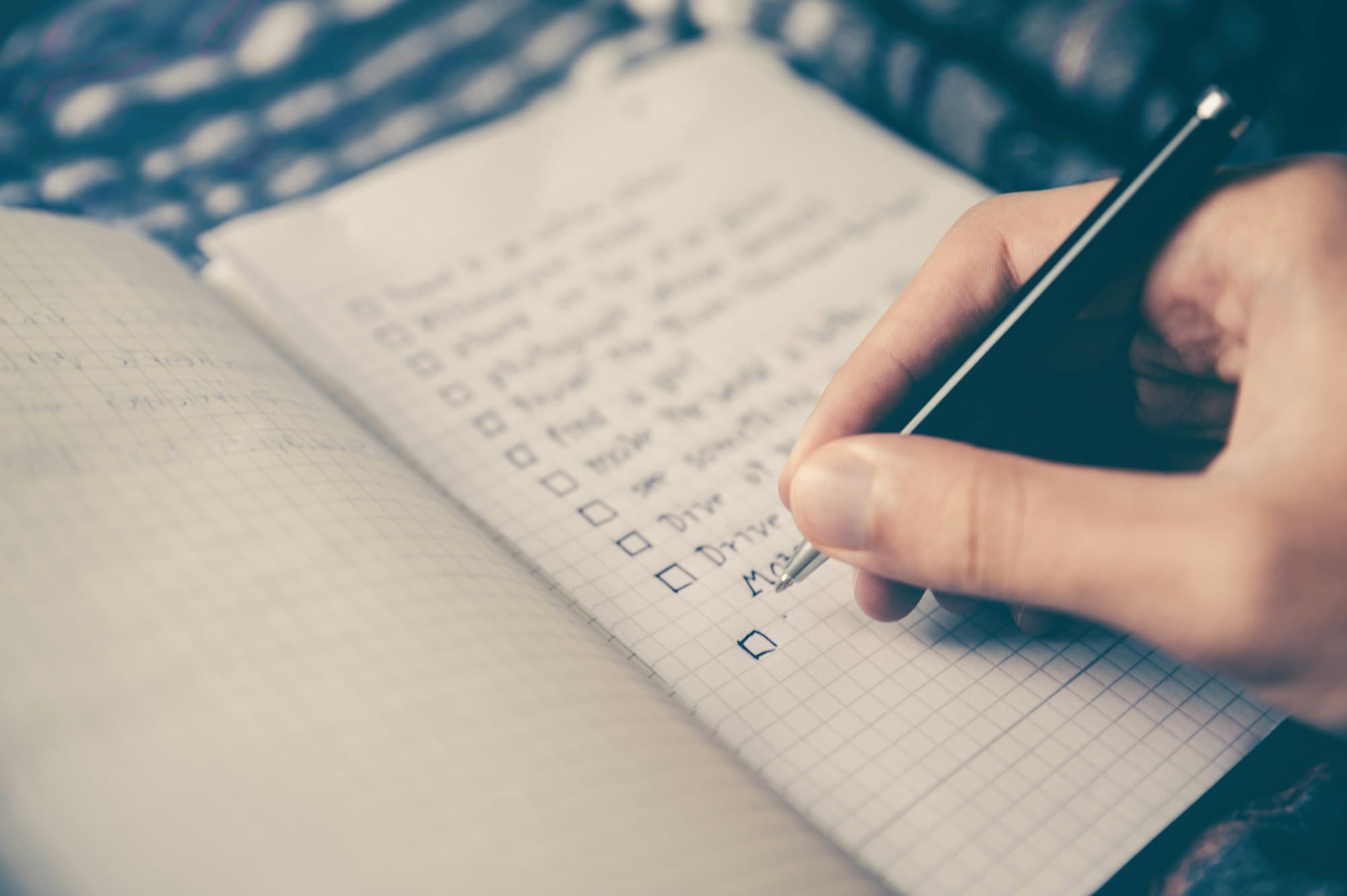 A hand holding a pen works down a handwritten checklist in a notebook