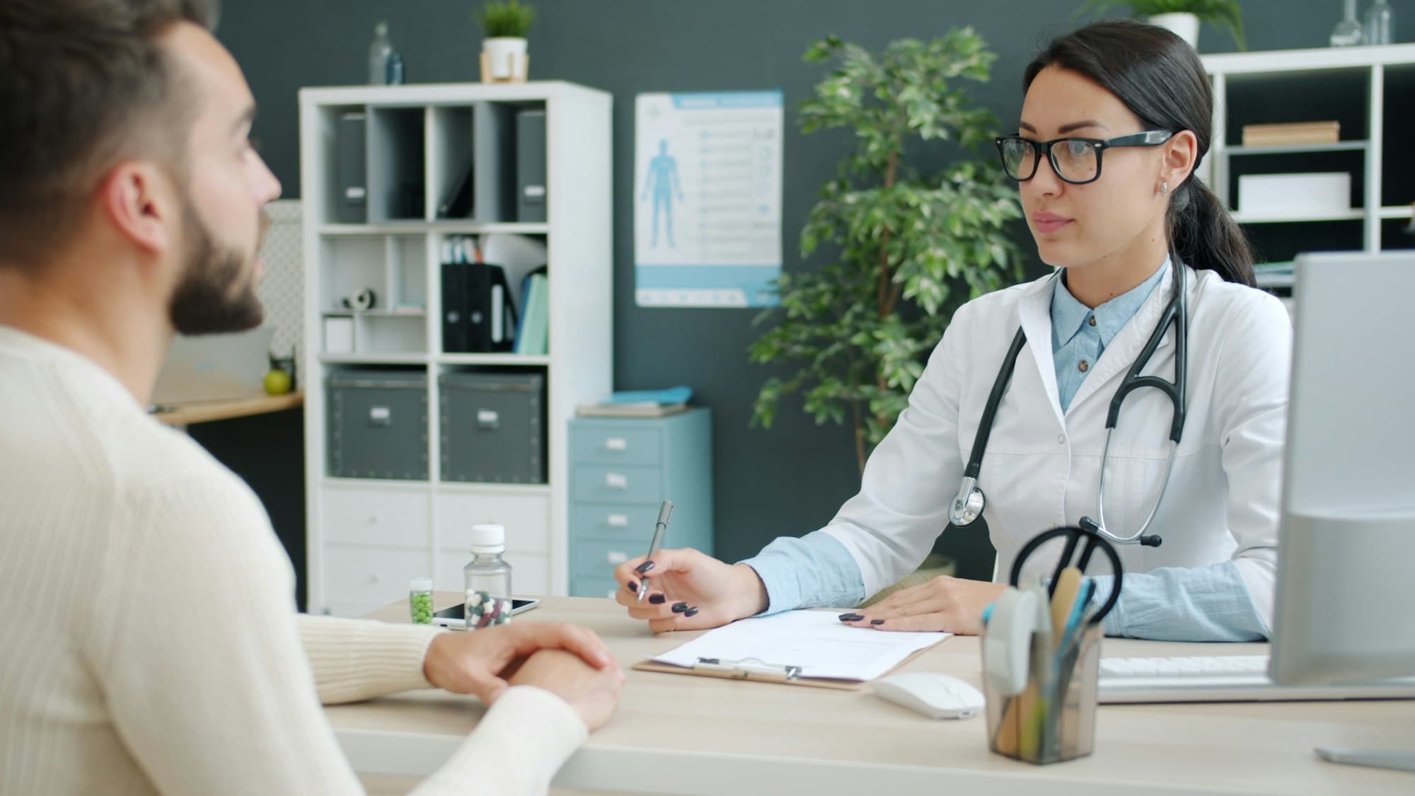 A physician and a patient talk across a desk in a small private office